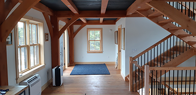 A brightly lit inside of a home showing warm, wood features like exposed beams and a staircase.