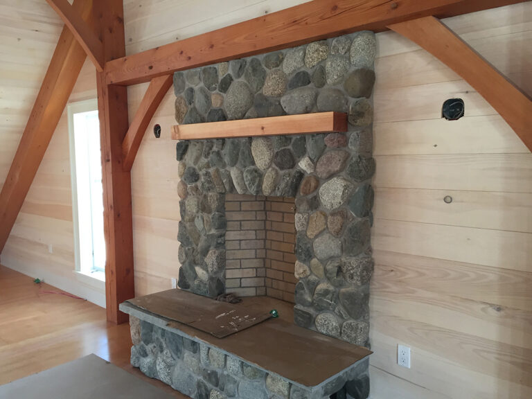 A stone fireplace is show indoors, surrounded by wood accents.